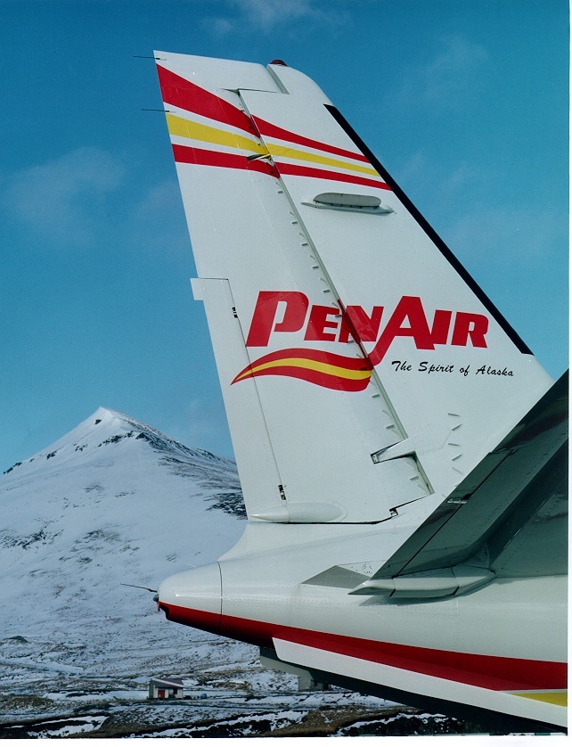 PenAir aircraft tail with red and yellow striping and snow-covered mountain in background.