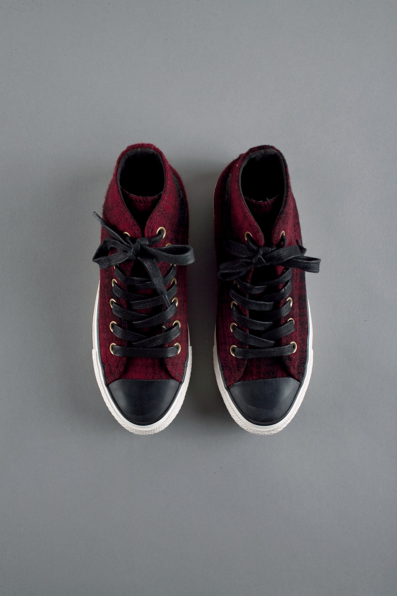 Pair of burgundy high-top sneakers with black laces and white sole, shot from above on grey background.