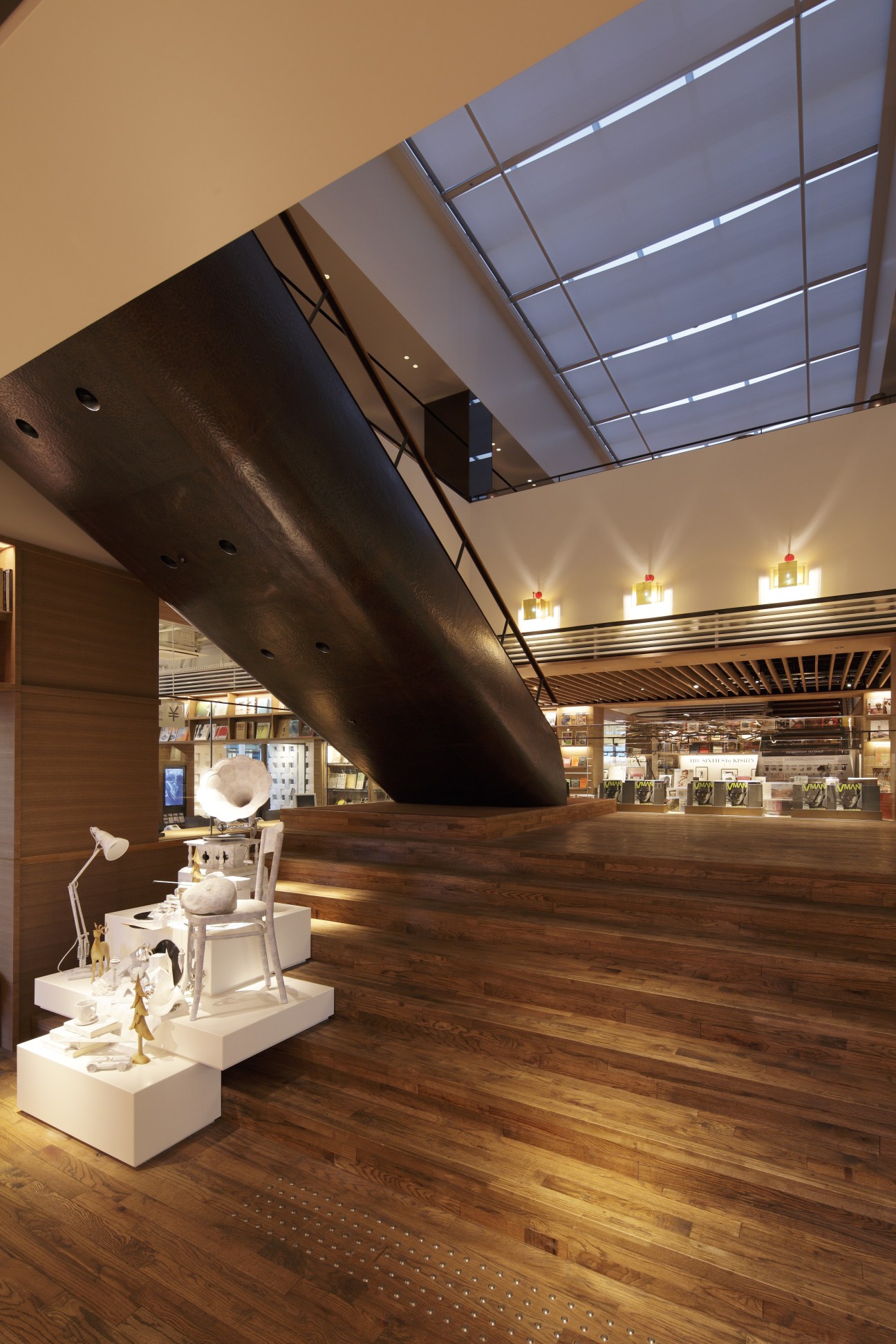 Modern stairway with dramatic curved black architectural element and wooden flooring leading to Tsutaya Books lounge.