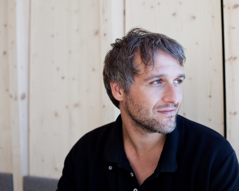 Portrait of architect Pavol Mikolajcak against a light wooden wall background.