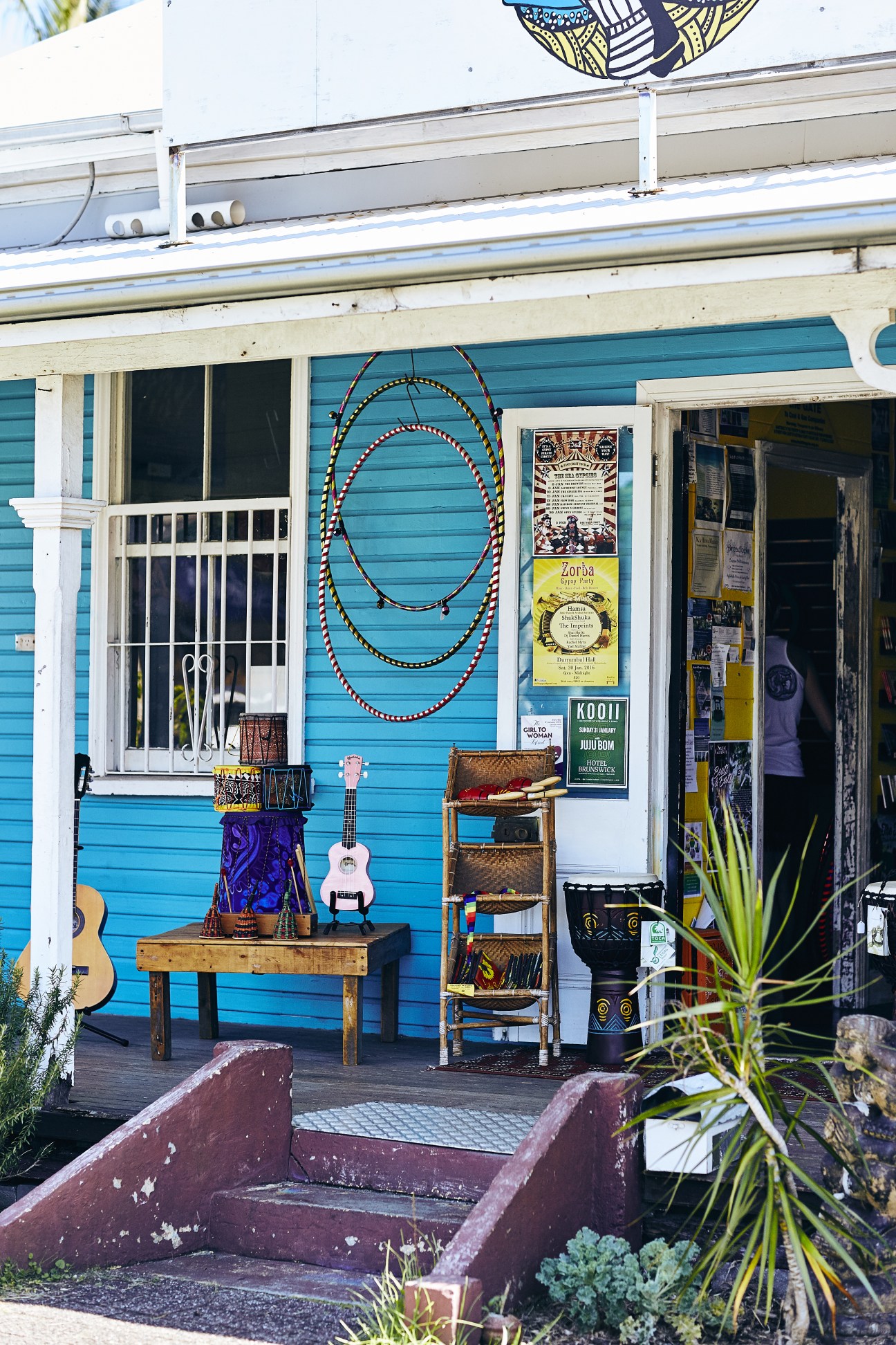 Turquoise storefront displaying musical instruments including guitars and didgeridoos with decorative beaded circles.