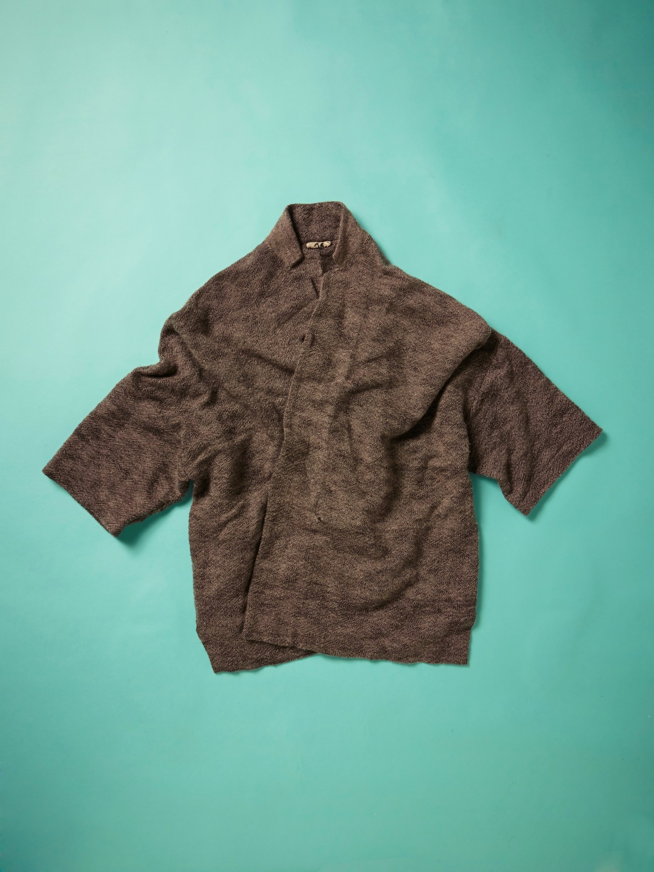 Brown merino wool shawl-collar sweater with short sleeves on turquoise background.