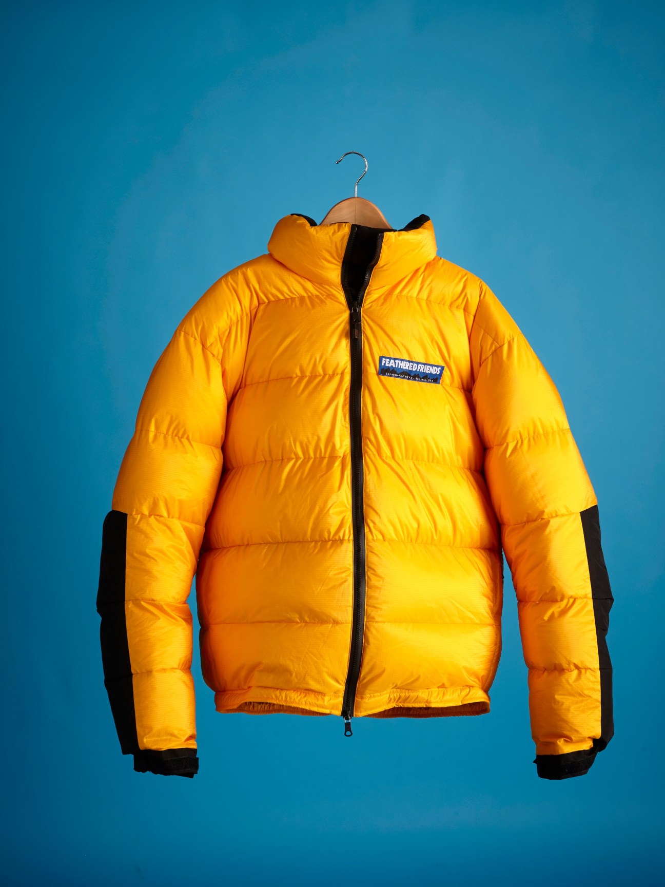 Feathered Friends Frontpoint jacket in yellow with goose down insulation and black trim on blue background