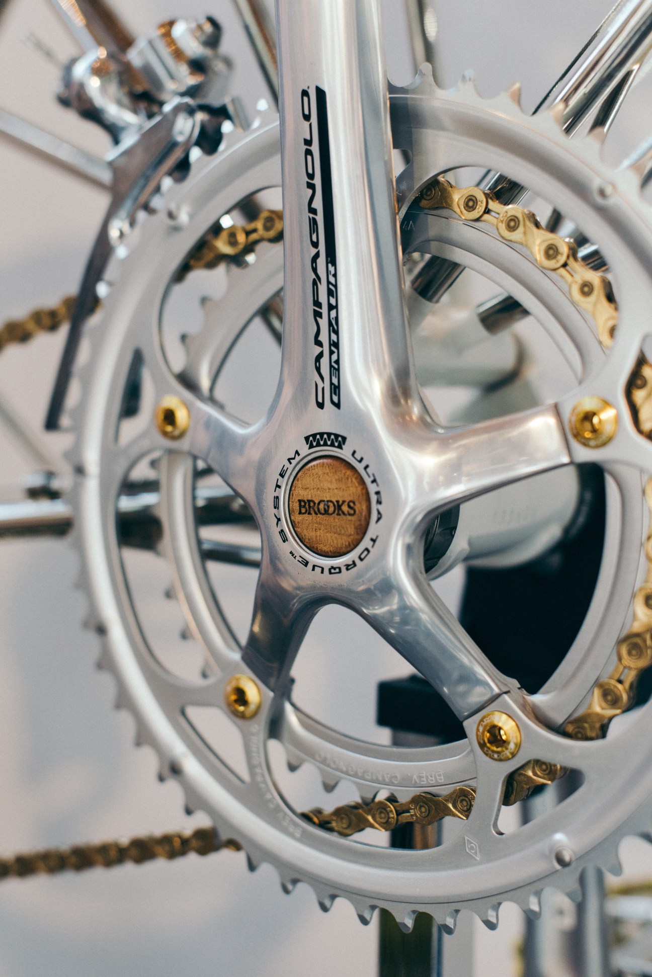 Close-up of white Campagnolo crankset with gold chain links and Brooks saddle detail on Moulton bike.