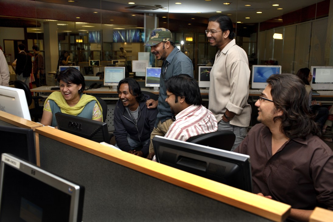 Dawn News team members laughing together at computer workstations in an office.