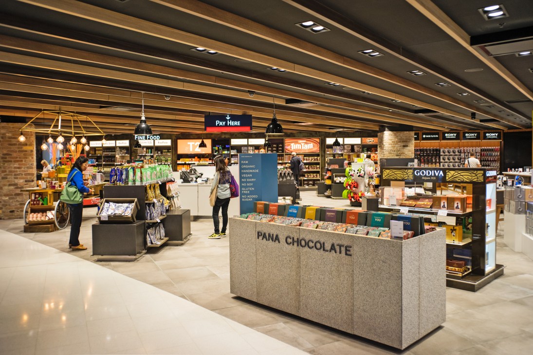 Modern duty-free shop interior at Sydney Airport with Pana Chocolate counter and various brand displays.