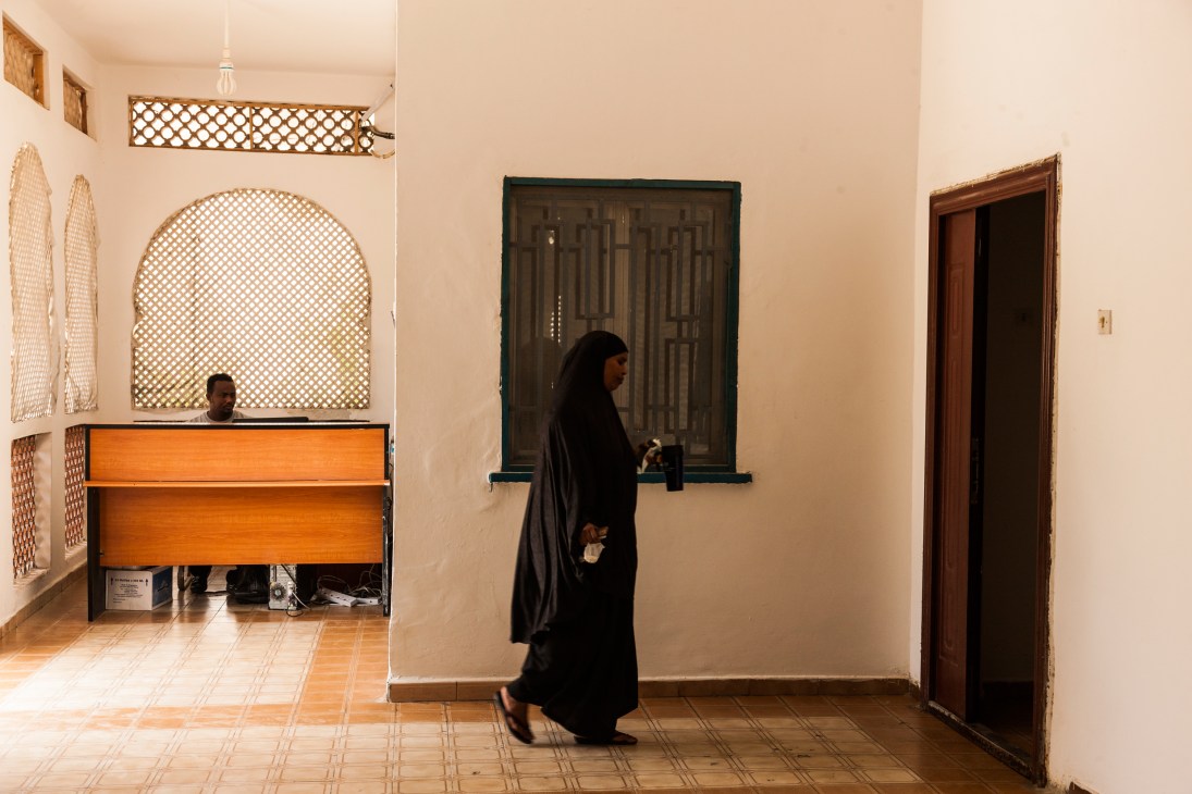 Woman in black clothing walking past an orange wooden desk in a hotel hallway with latticed window screens.