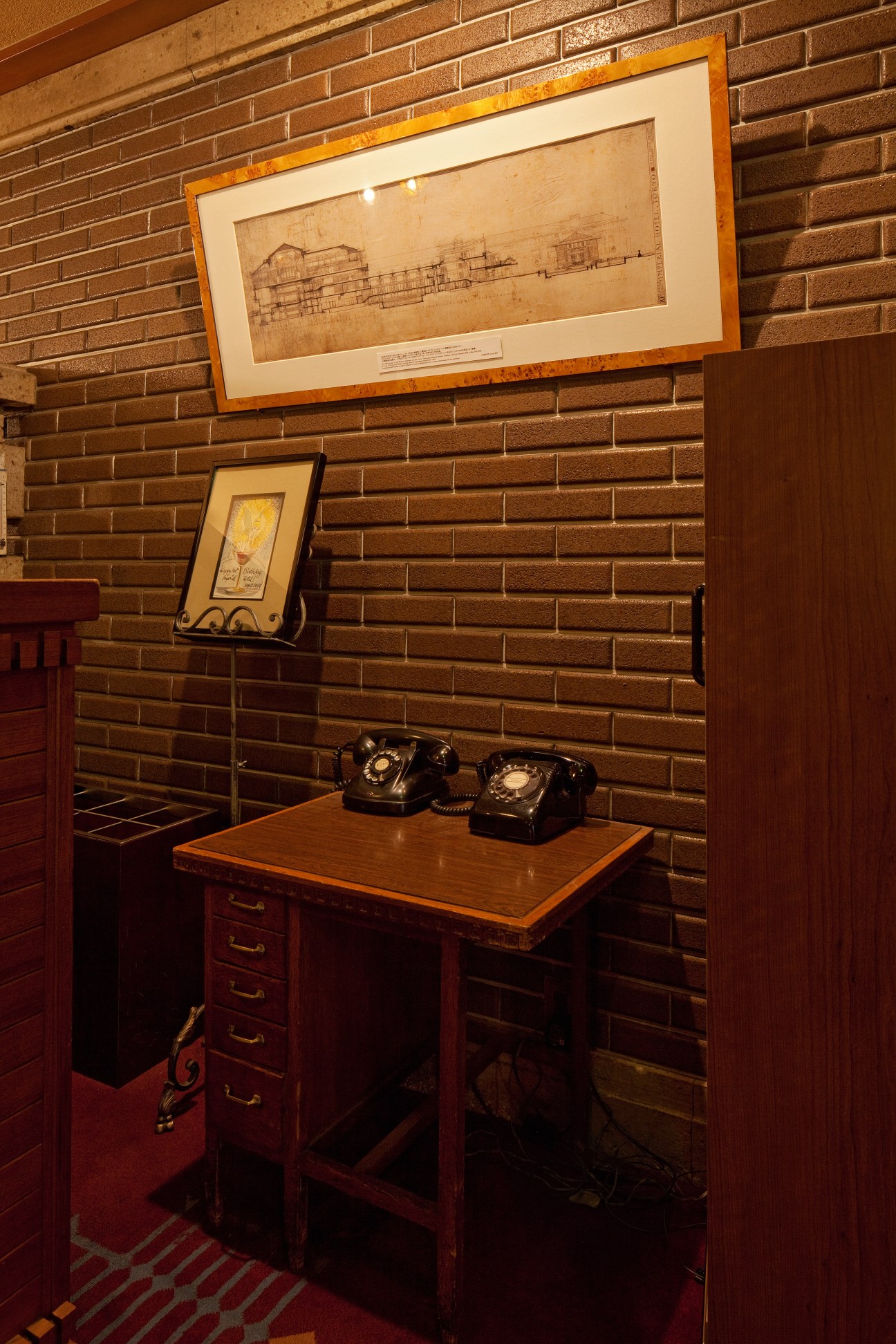 Vintage desk with two black rotary phones and framed architectural drawings on brick wall at Old Imperial Bar.