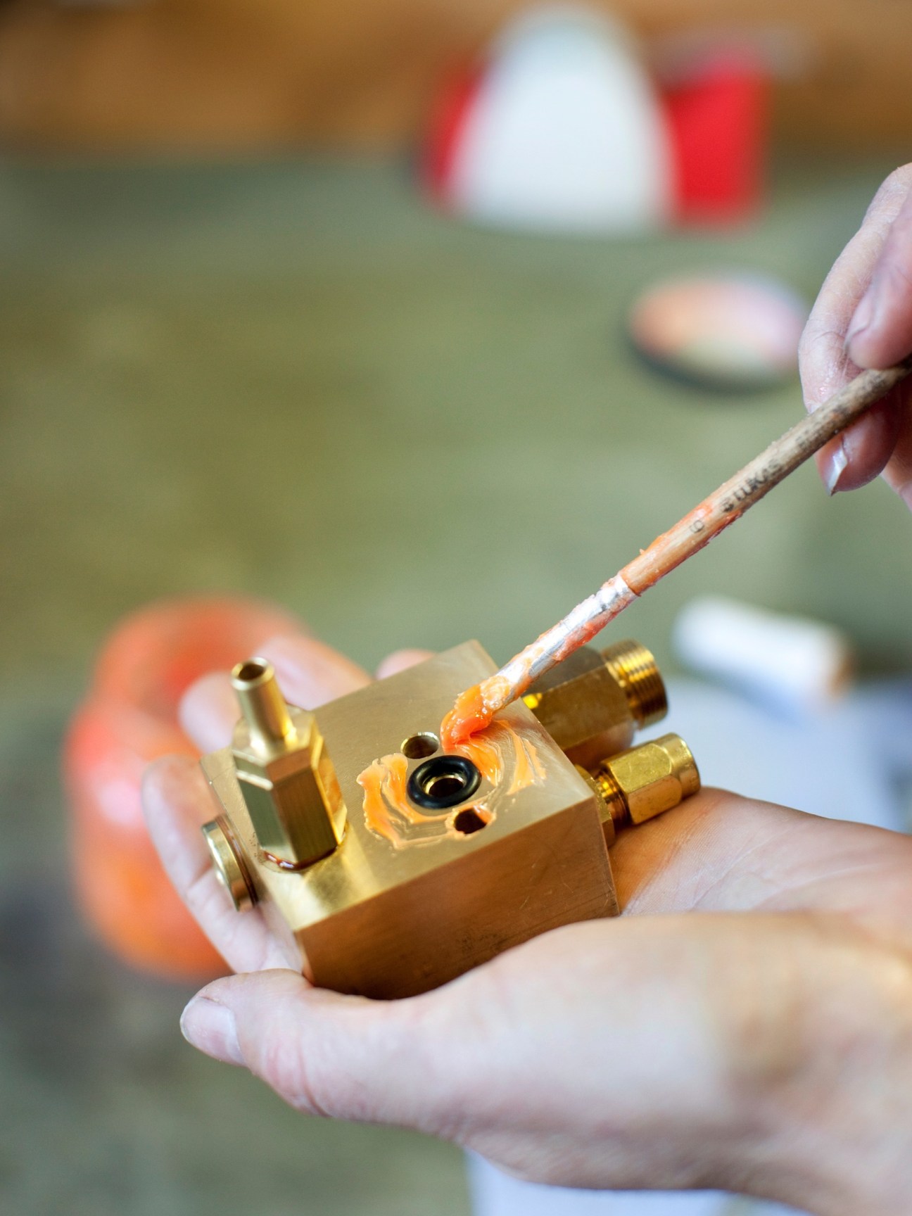 Worker's hands soldering a brass espresso machine component with a torch.