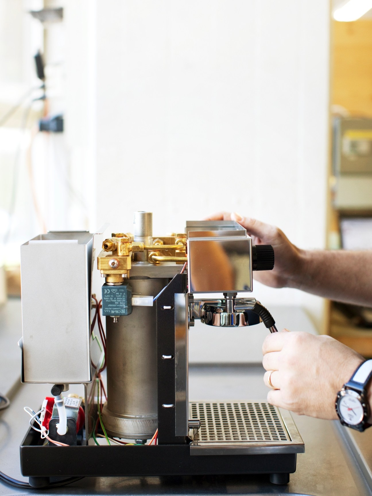 Hands assembling an Olympia espresso machine with visible brass fittings and metal components during testing.