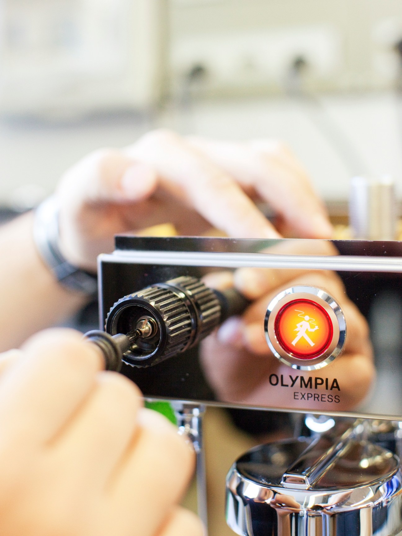 Hands assembling an Olympia Express espresso machine with its distinctive red logo featuring a running waiter.