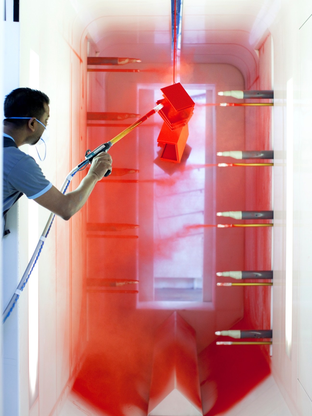 Worker spray-painting red espresso machine parts inside an industrial spray booth.