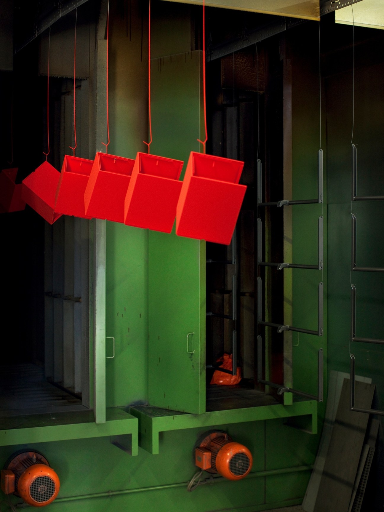 Industrial painting station with bright red espresso machine parts suspended by cords above a green industrial machine.