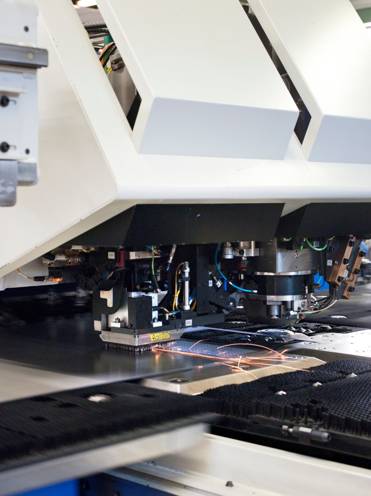 Laser cutting machine TruMatic 6000 cutting metal sheets with sparks visible during Olympia espresso machine manufacturing.