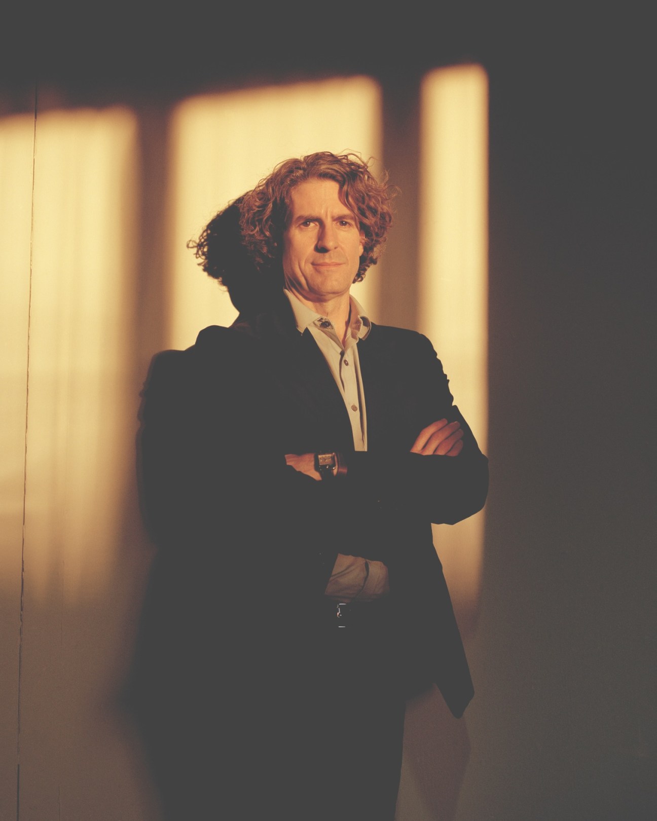 Portrait of Richard Wright, Chicago auctioneer, standing with arms crossed against illuminated backdrop.