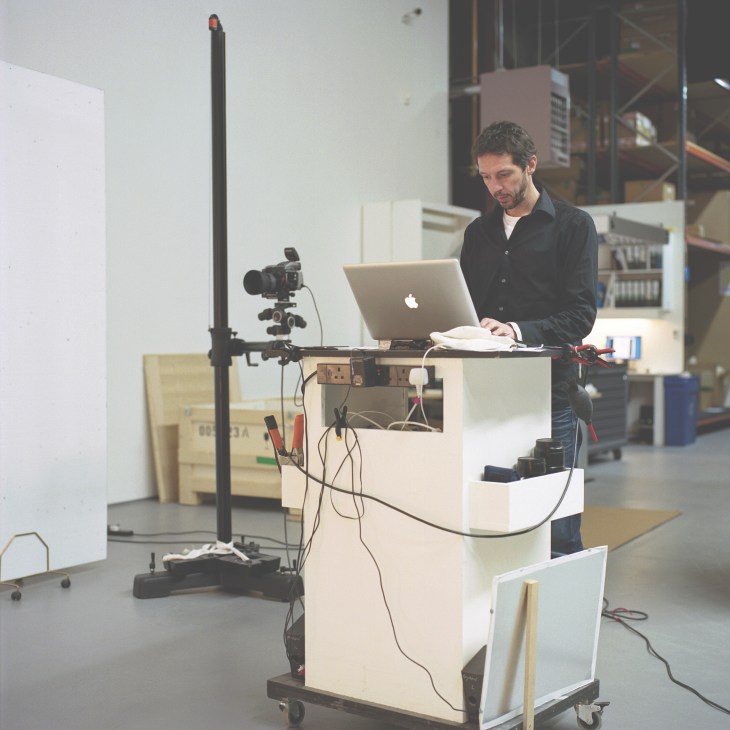 Photographer Byron Slater working at a laptop with professional camera equipment on a studio setup.