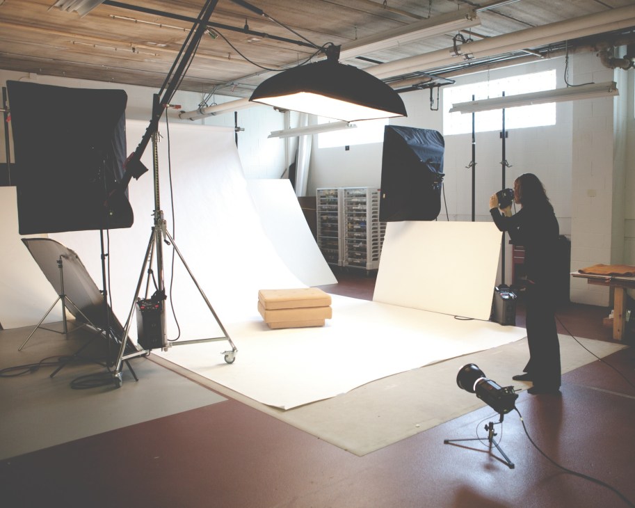Professional photography studio with lighting equipment, white backdrop, and photographer at work