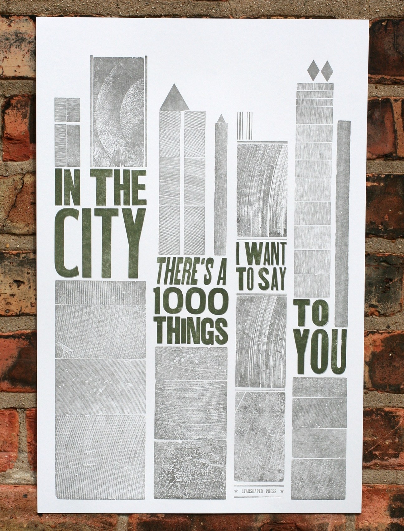 Letterpress poster with stylized city buildings and text 'In the City There's a 1000 Things I Want to Say to You' by Starshaped Press on brick background.
