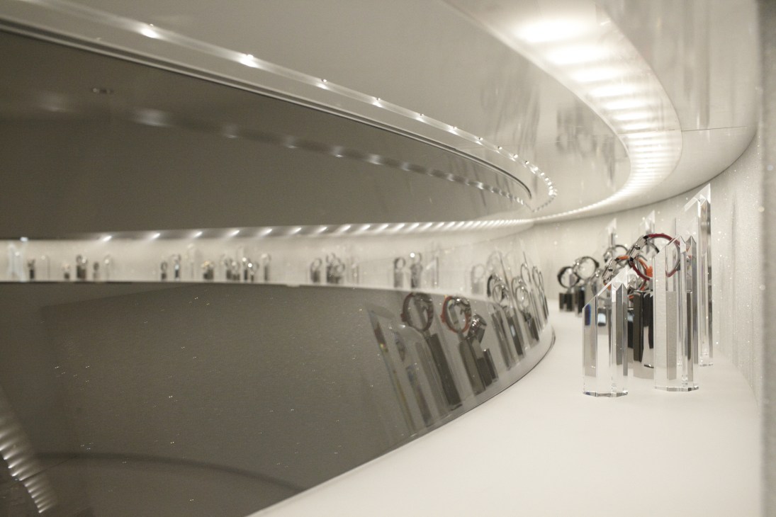 Luxury watches displayed on curved white shelving in a modern retail showroom with recessed lighting.