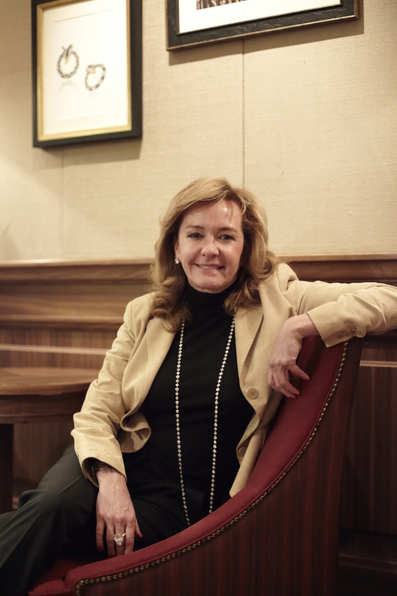 Caroline Gruosi-Scheufele, Chopard co-president, seated in wood-paneled showroom with framed watch designs on wall behind her.