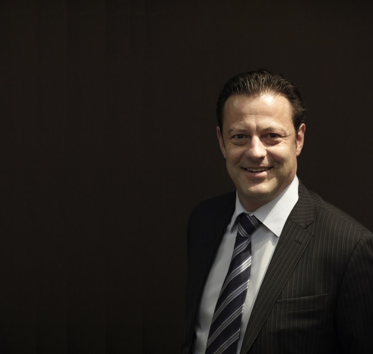 Portrait of Antoine Martin CEO Bruno Jufer in a dark pinstriped suit and striped tie against a black background.