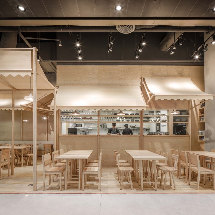 Light ash wood interior of Eat Rice & Noodles restaurant with trestle tables, wooden chairs, and canvas awnings.