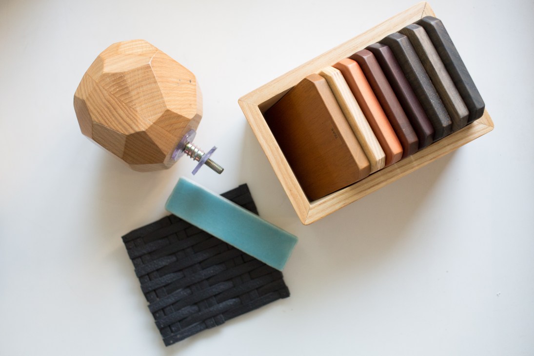 Material samples including ceramic tiles, timber swatches, PVC, and a geometric wooden doorknob in a natural wood box.