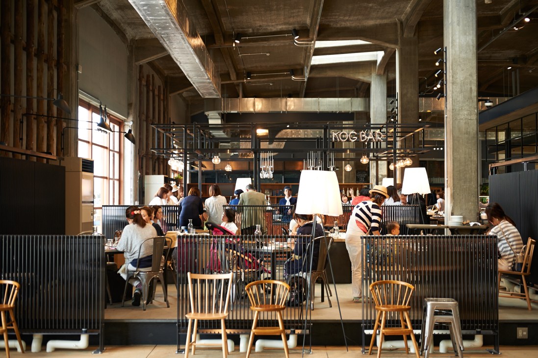 The Restaurant at Onomichi U2, a converted warehouse space with industrial ceilings, wooden chairs, and diners seated at tables.