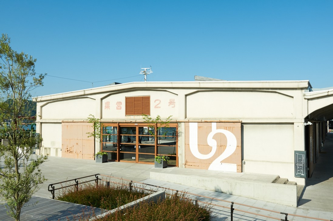 Exterior of Onomichi U2 complex with converted warehouse featuring wooden doors and large white numeral 2 signage.