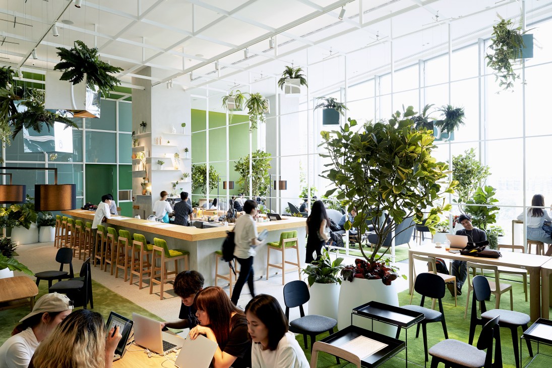 Bright modern co-working space with green plants, wooden tables, and floor-to-ceiling windows at Open House Bangkok.