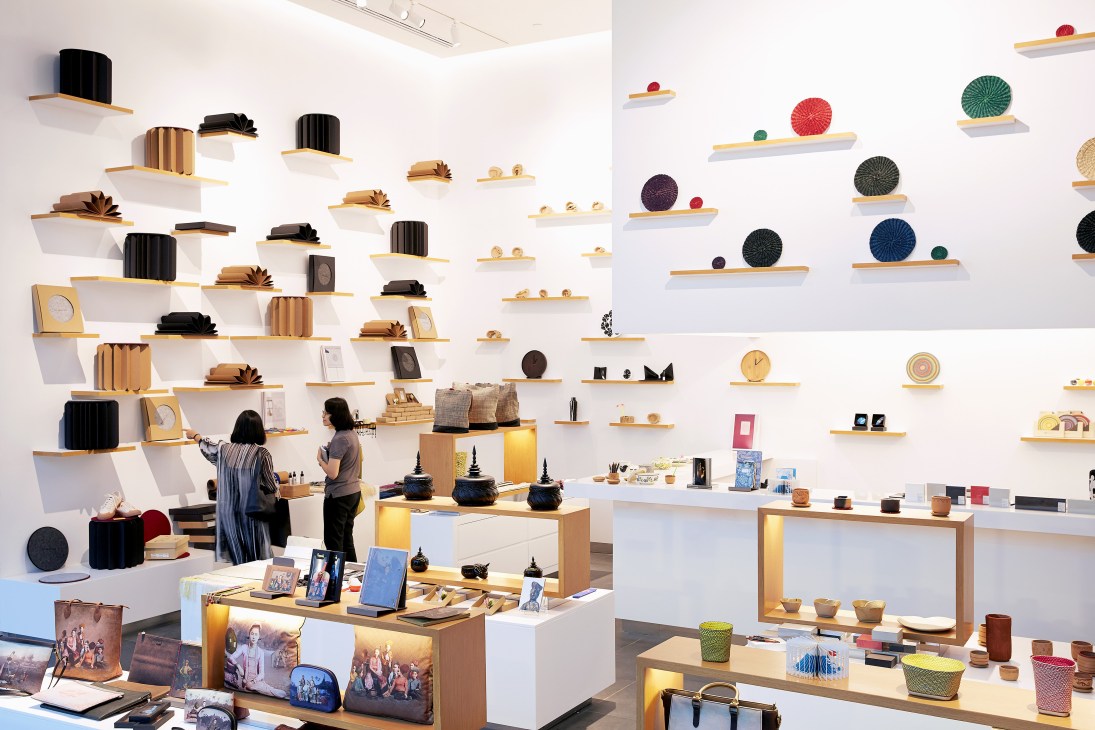 White-walled retail display featuring wooden shelves with black cylindrical objects, colorful spheres, and design products curated by Open House in Bangkok.
