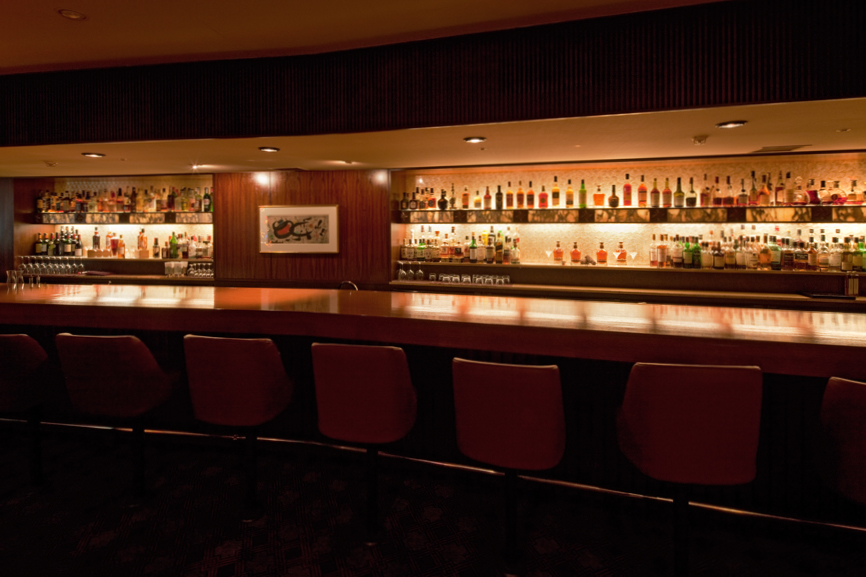 The Orchid Bar at Hotel Okura with burgundy bar stools, wood paneling, and illuminated shelves of spirits.