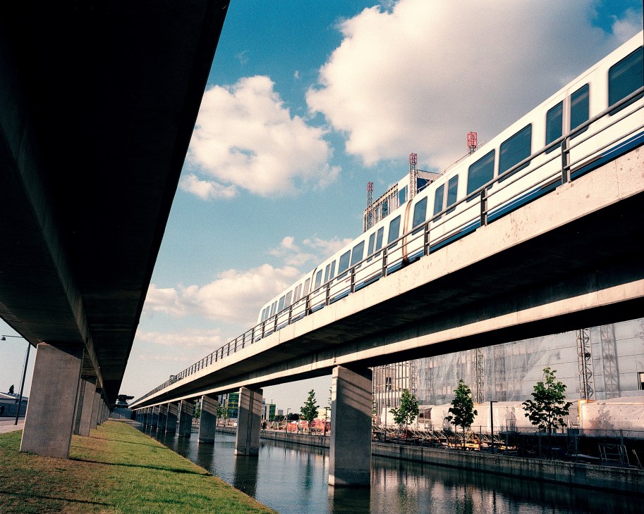 Copenhagen's elevated metro train crossing over a canal in the Ørestaden district with modern architecture and clear sky.