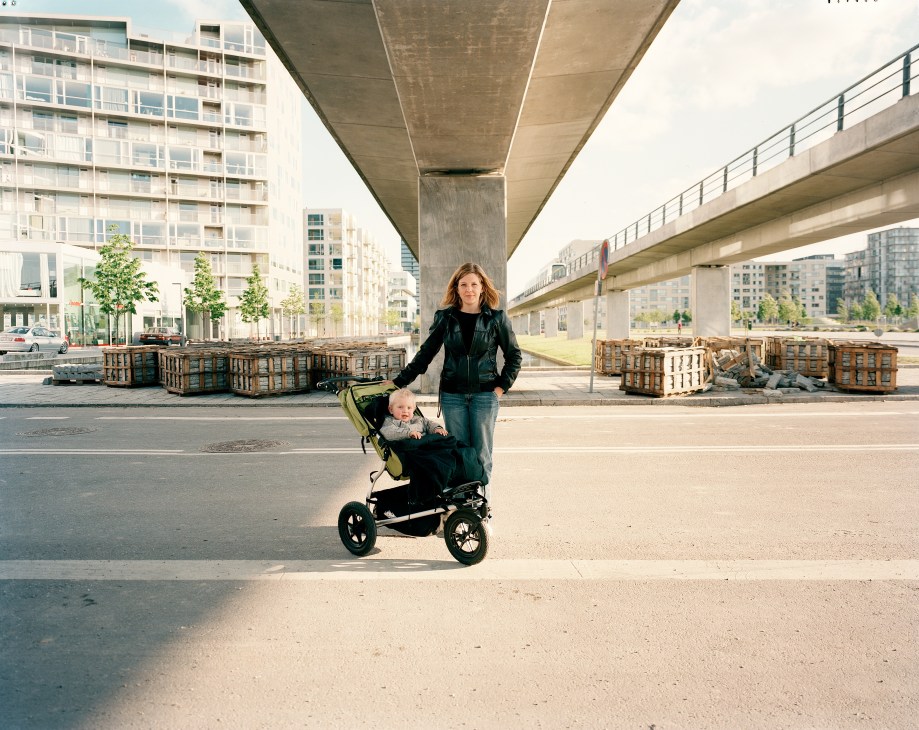 Woman with child in stroller under elevated highway in Ørestaden, Copenhagen.