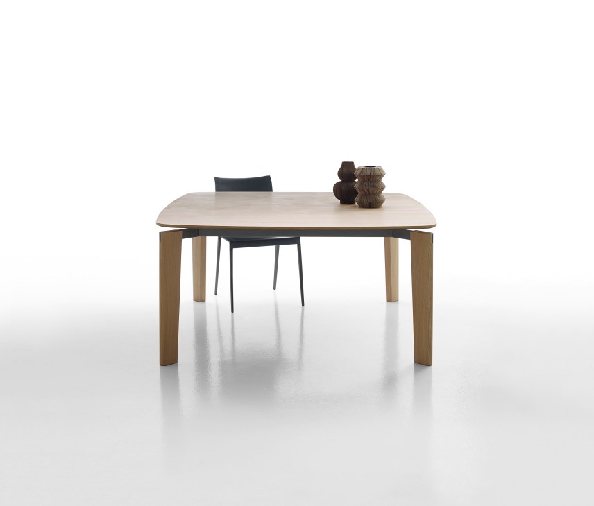 Oskar table by Vincent Van Duysen featuring a light wood top and wooden legs with a black chair and decorative objects.