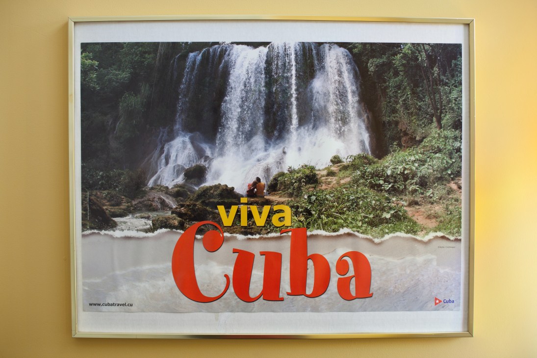Framed Cuba travel poster with waterfall image hanging on yellow wall