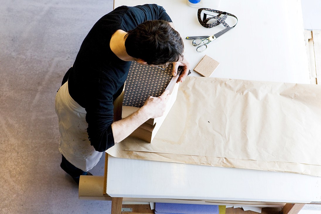 Artisan gluing monogrammed canvas to the exterior of a Moynat trunk.