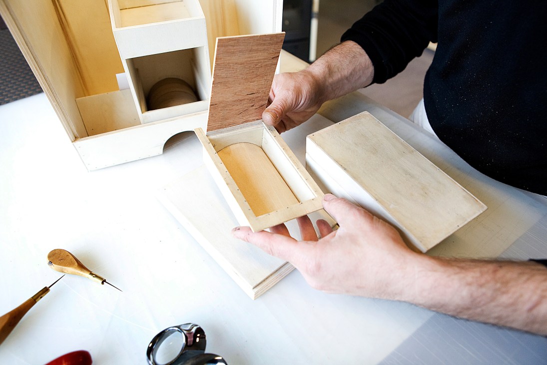 Artisan's hands assembling wooden compartments and drawers for a luxury trunk.