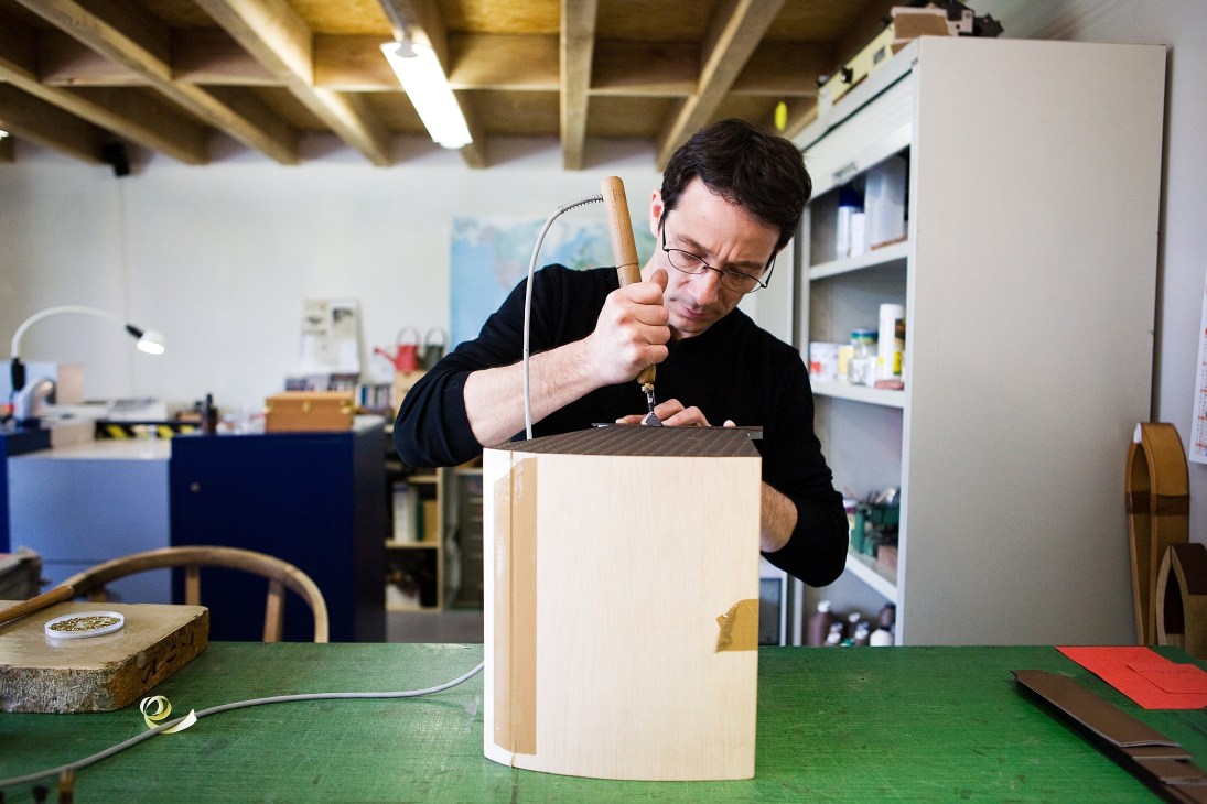 Craftsman using an awl to perforate leather on a wooden trunk in a workshop
