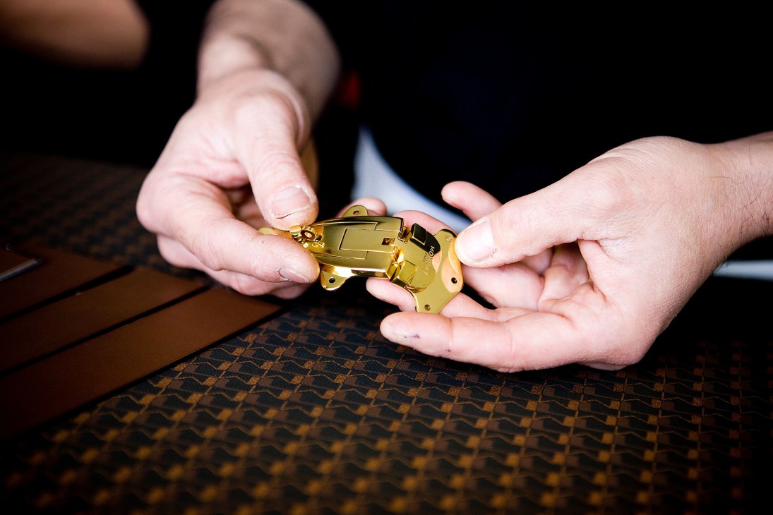 Two hands holding a brass clasp lock for a Moynat trunk.