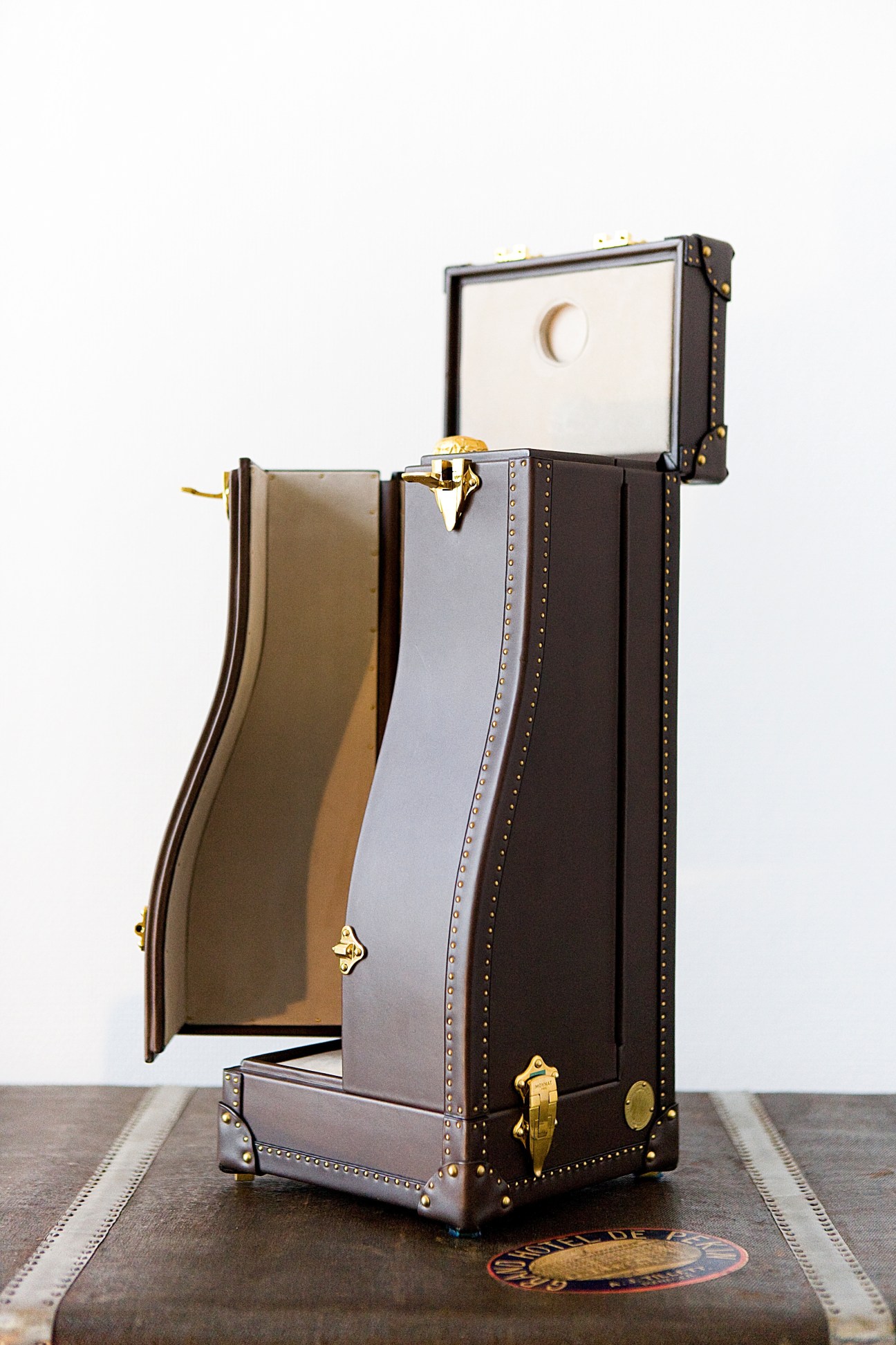 Open Moynat Malle Krug champagne trunk with dark leather exterior, brass hardware, and cream-colored interior compartments.