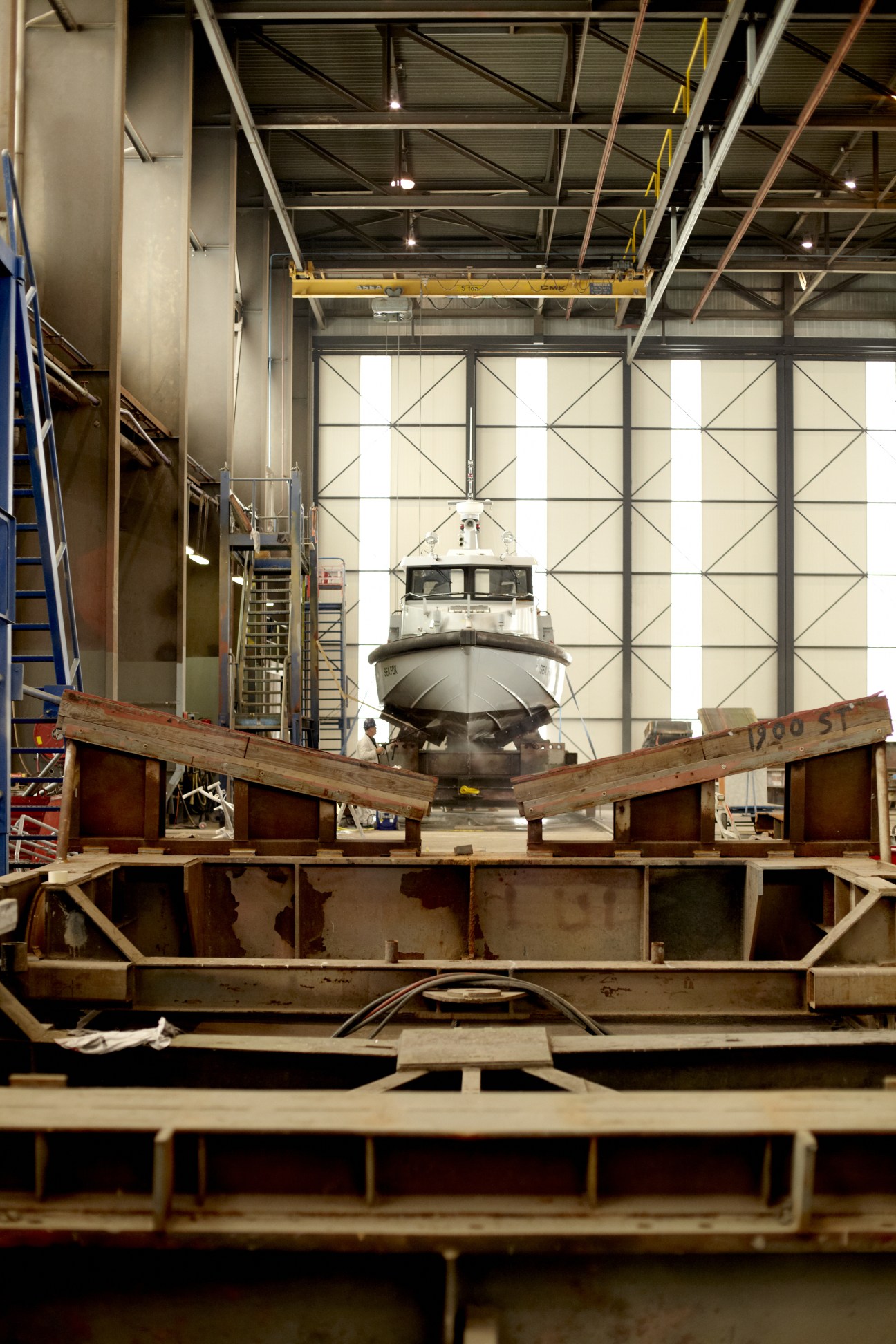 A Stan Patrol 1204 boat under construction in a Damen shipyard factory with overhead crane and large windows.