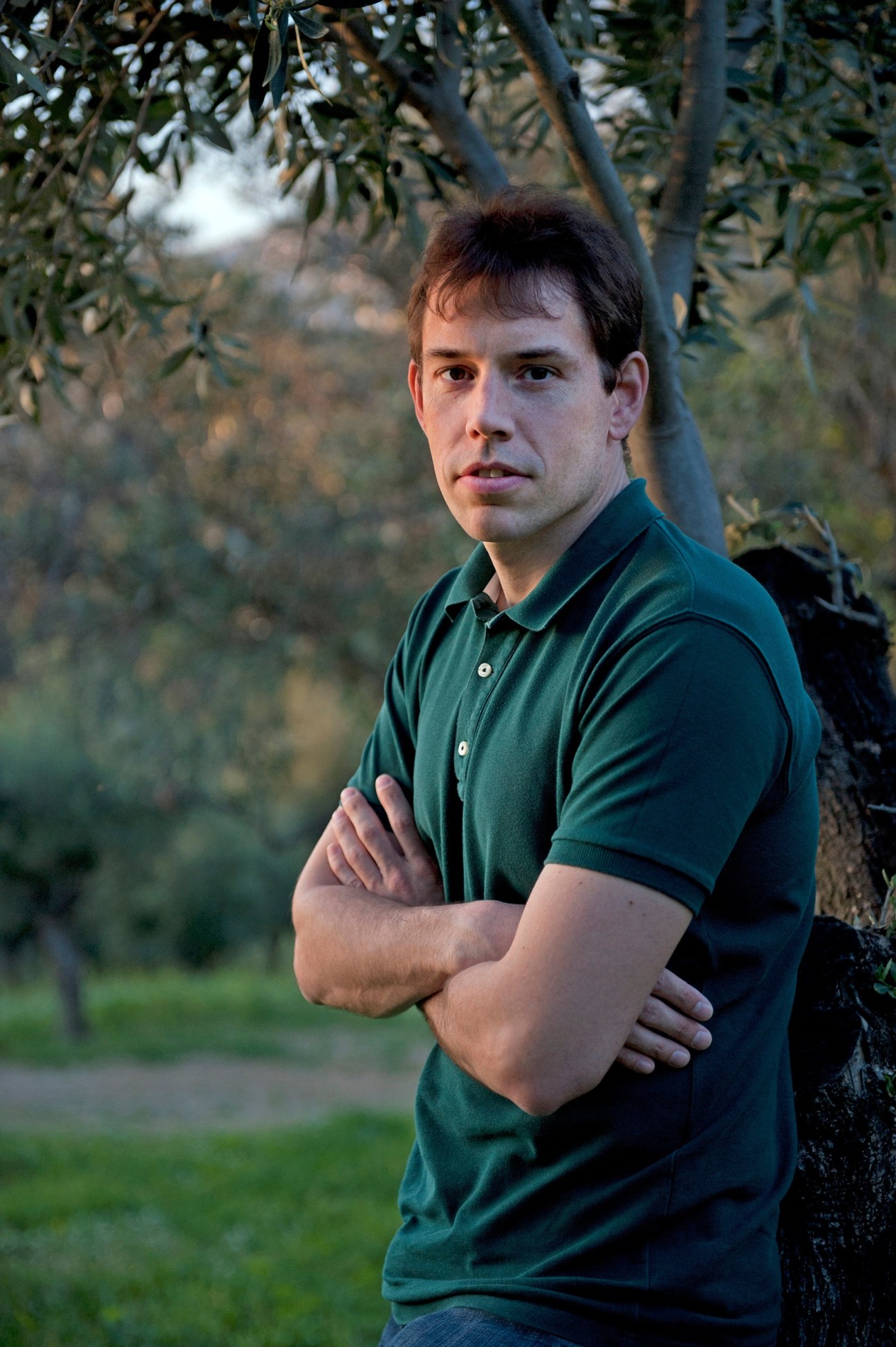 Kostas Theodoropoulos, founder of O2 Olive Oil, standing beneath olive tree branches.
