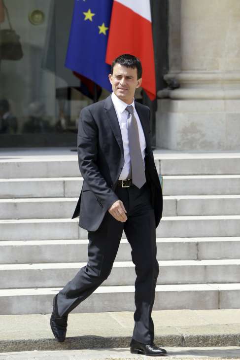 Manuel Valls walking down steps in front of French and EU flags.