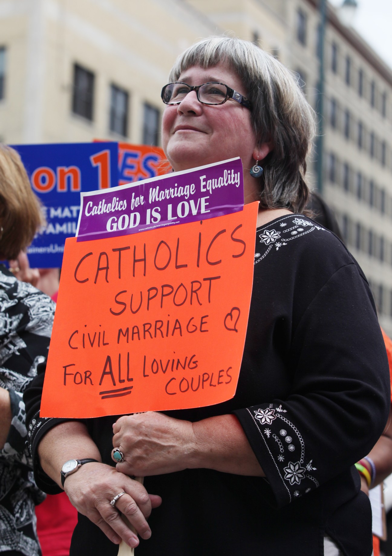 Woman wearing glasses holding signs supporting same-sex marriage at a protest rally.