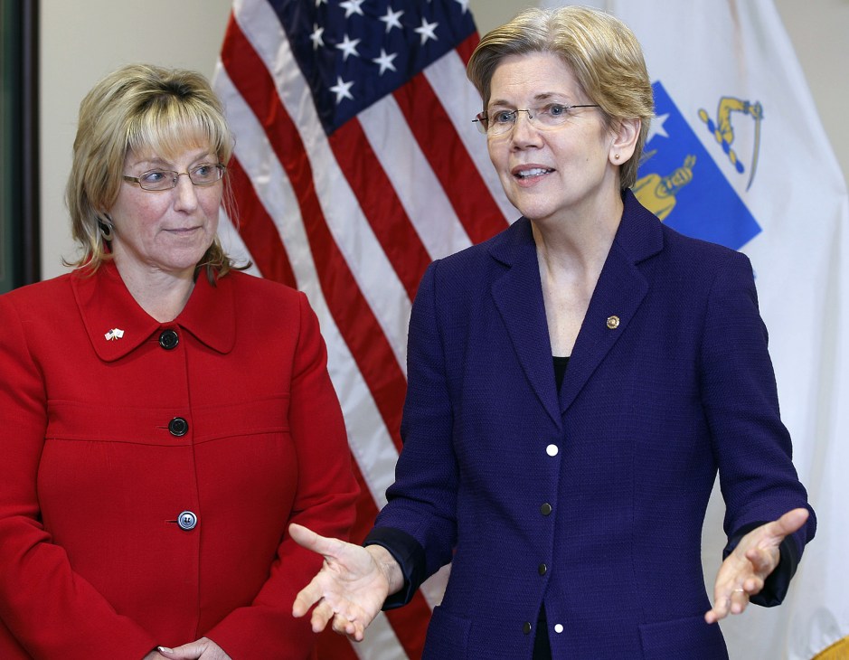 Elizabeth Warren in navy blazer speaking with another woman in red jacket before American flag.
