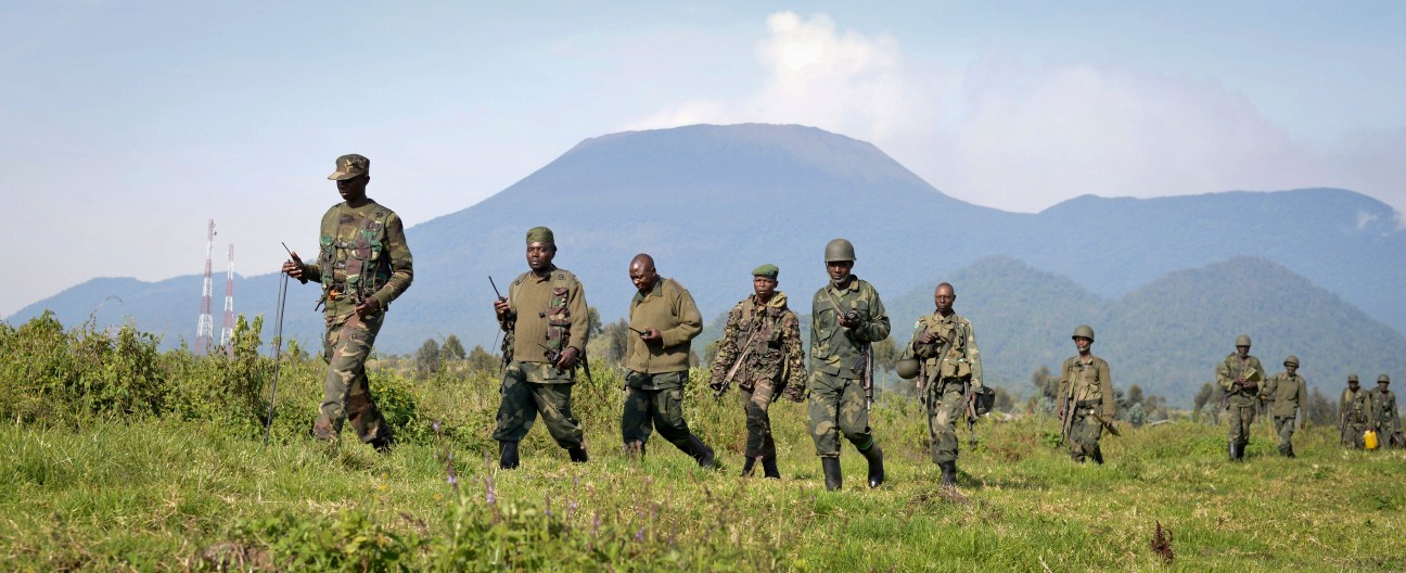 Democratic Republic of Congo army soldiers marching through a grassy field with mountains in the background.