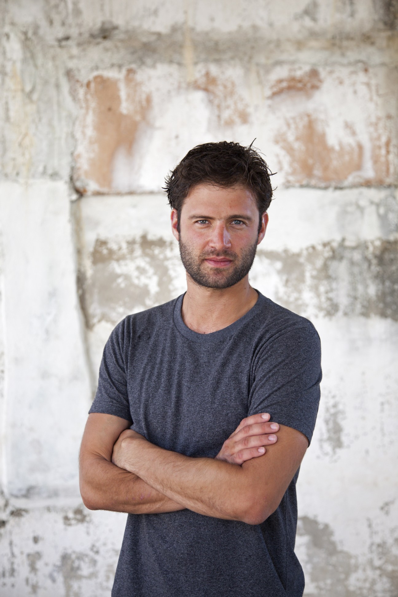 War photographer Sebastian Meyer poses with arms crossed against a weathered whitewashed brick wall.