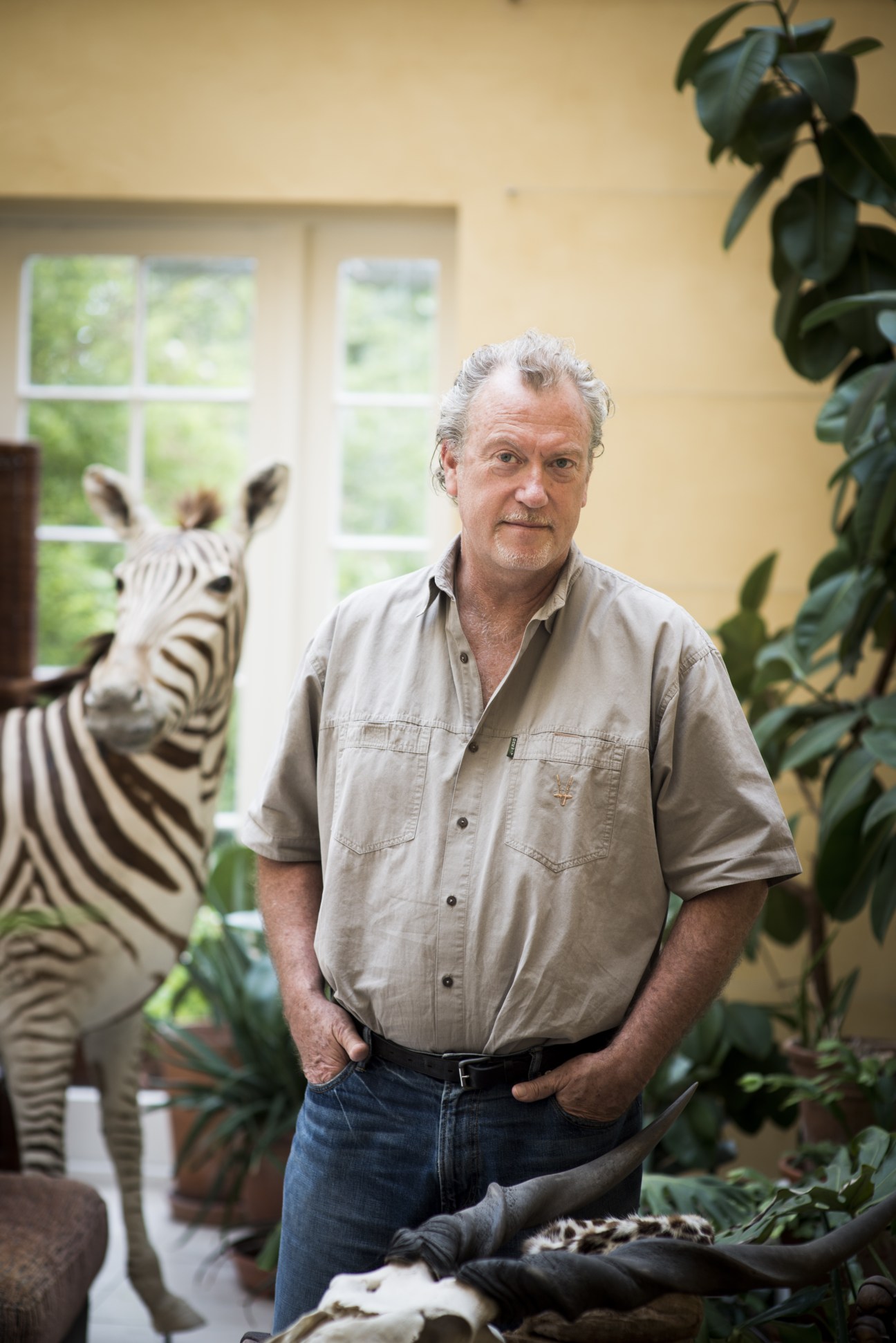Jon Lee Anderson, New Yorker staff writer, stands indoors with a zebra mount and potted plants behind him.
