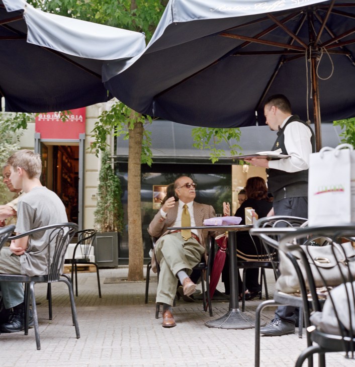 Waiter serves customers seated under black umbrellas at Antico Caffe Spinnato's outdoor terrace in Palermo.